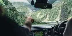Hand pointing forward from the front seat of a car as two people drive down a steep road in the South Island