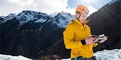 Image of a climber in the snow on a mountain wearing a helmet and looking at a map - mobile