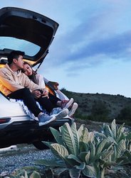 Image of a couple sitting in the back of their 4x4 rental car at dusk