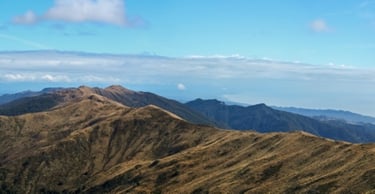 Panoramic view of golden mountain ridges under a blue sky with the ocean in the distance