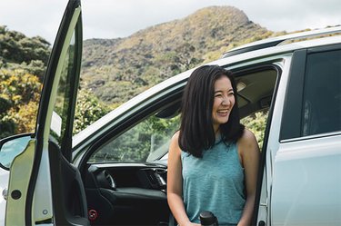 Image of woman laughing, sitting on the front seat of car parked in front of dense bush