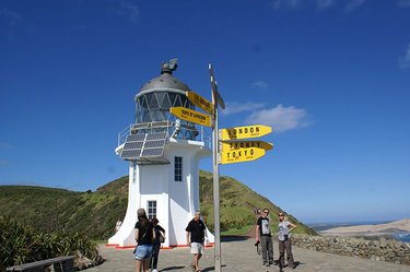 Image of the Cape Reinga Lighthouse on a sunny day with the world destination sign in the foreground