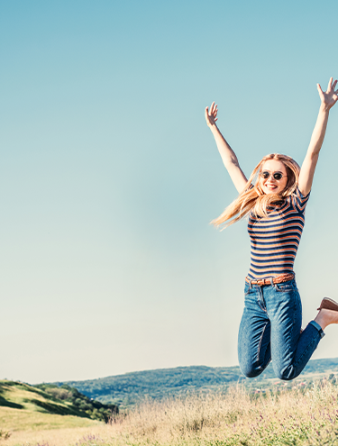 A girl in jeans jumping up next to her car 