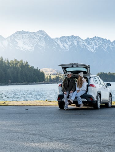 A man and a woman sit in the back of a GO Rentals Toyota Corolla Cross Hybrid car talking and sharing memories