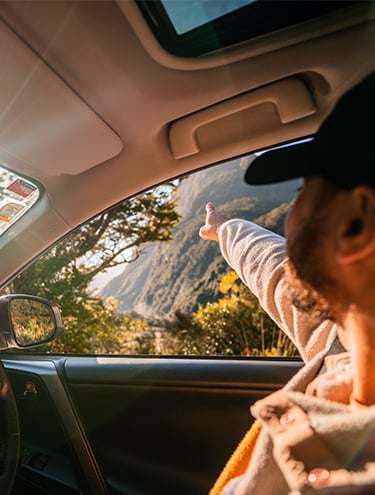 A guy with cap pointing out the view outside of the car window