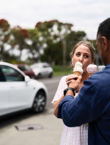 A family is having ice-cream on the road by the white car 