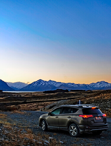 Image of a Toyota Rav4 at dusk overlooking the lakes and mountains of the South Island