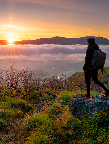 Image of a male stood on a rock at the top of a mountain overlooking a landscape covered in cloud