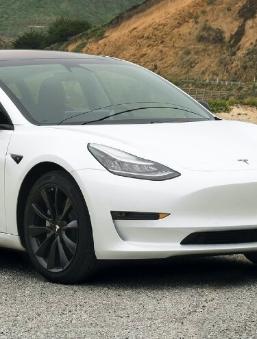 White Tesla Model 3 parked with mountain in the background