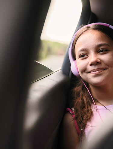 Image of a girl sitting in the backseat with her headphones on looking outside the car window and enjoying her journey with GO Rentals