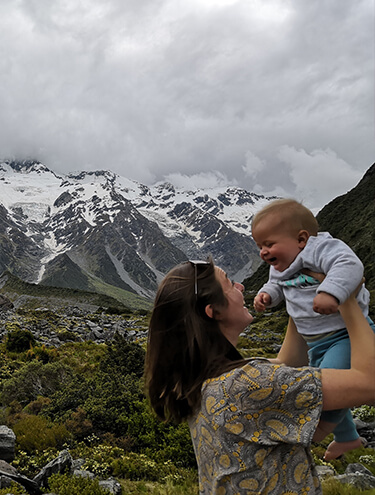 Image of a female holding up a baby and smiling with snowy mountains in the background