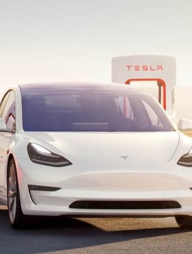 Front view of a Tesla vehicles parked next to a Tesla Supercharger station