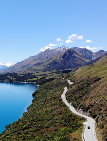 Image of a lake, mountains and road in the background with a car in the foreground