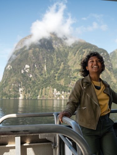 Smiling woman enjoying a scenic boat ride through a fjord surrounded by lush green mountains