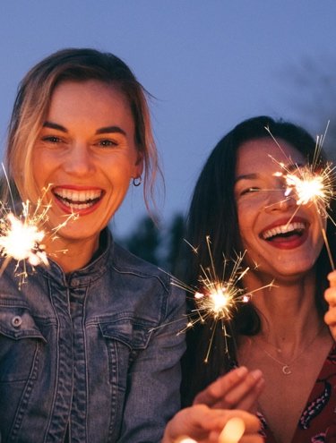 Group of friends smiling and holding sparklers at night during a celebration