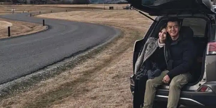 A couple sitting in the open trunk of a car by a winding country road