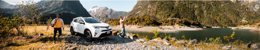 White SUV parked by a mountain lake with two people enjoying the scenic view