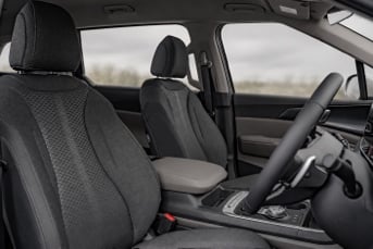 Interior image of the front of a Kia Carnival Hybrid showing the driver and passenger seats, dashboard and steering wheel