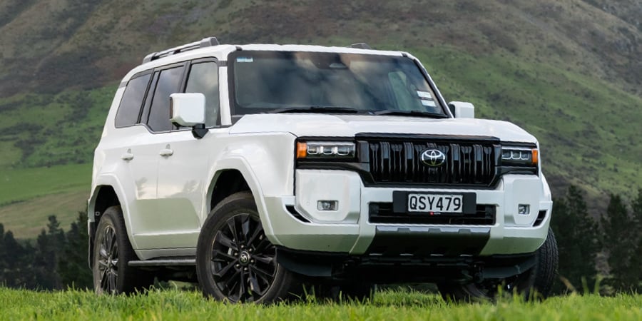 Front image of a Toyota Land Cruiser Prado Hybrid 4x4 with trees and a mountain in the background