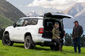 Side image of a Toyota Land Cruiser Prado Hybrid 4x4 parked on a grassy mountainside with a view of a lake in the distance