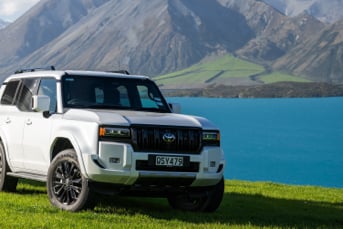 Front image of a Toyota Land Cruiser Prado Hybrid 4x4 parked on a grassy mountainside with a view of a lake in the distance
