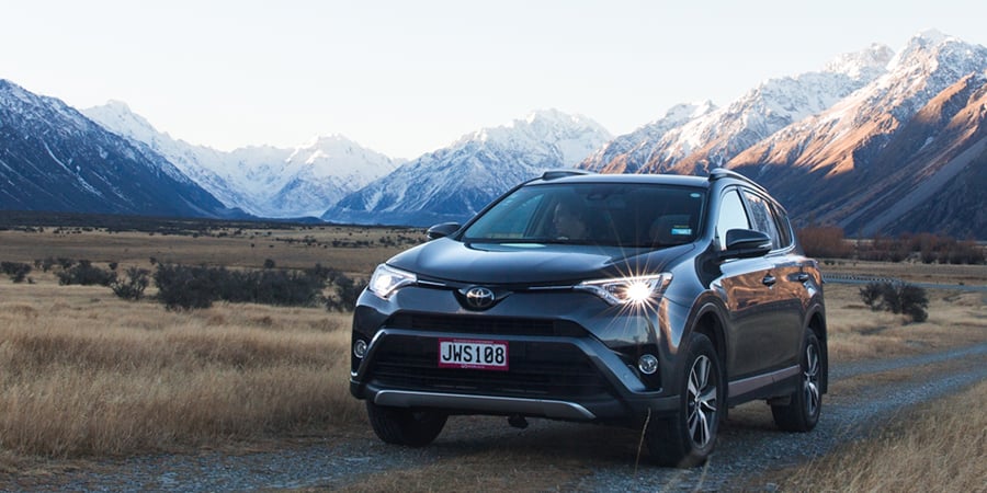 Exterior image of a Toyota Rav4 rental car parked off-road with snow-capped mountains in the backdrop
