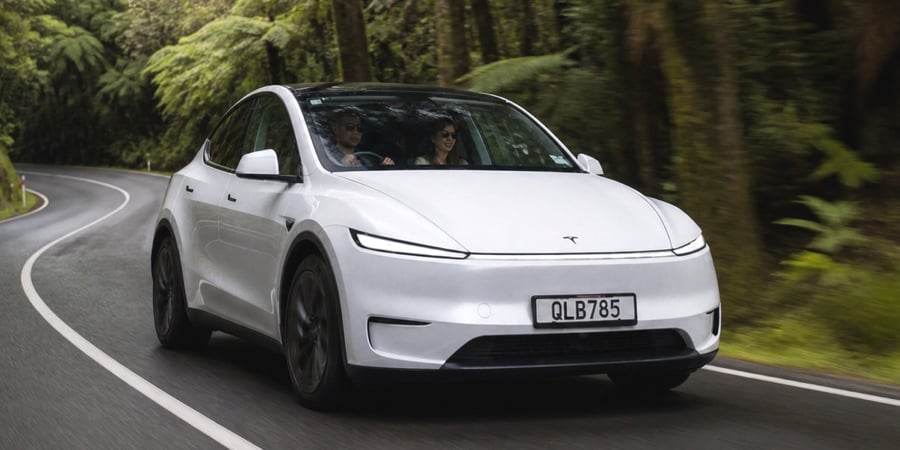 White Tesla Model Y L driving on a winding forest road with two people inside