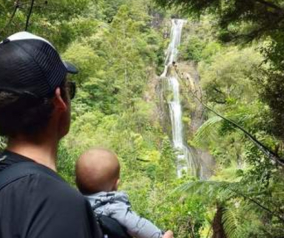 Greg holding a baby looking at a waterfall in New Zealand