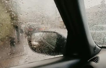 Rain-covered car window with blurred traffic outside