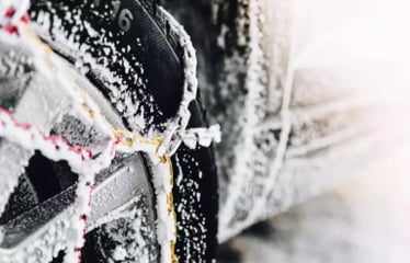 Close-up of a car tire with snow chains covered in ice and snow