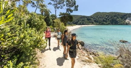 People hiking along a coastal trail with turquoise water and forest around