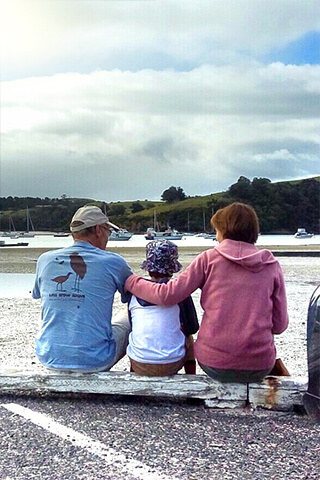 Image of a family sitting on a log at the beach with their backs to the camera