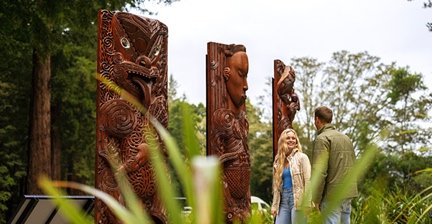 Couple admiring traditional Māori carvings in a lush Rotorua forest