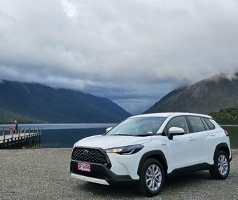 White SUV parked near a calm lake with mountains and clouds