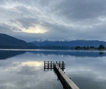 Wooden dock extending into a calm lake with mountains and clouds in the background