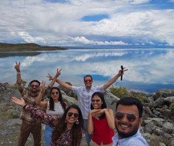 Group of friends taking a selfie by a clear lake with reflections of clouds