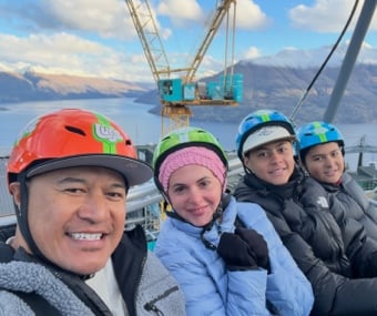 Four people wearing helmets, smiling at the camera with mountains and a crane in the background