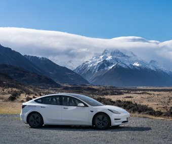 White Tesla parked in a scenic valley with snow-capped mountains