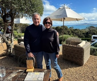 A couple standing together outdoors at a cafe with ocean views behind them