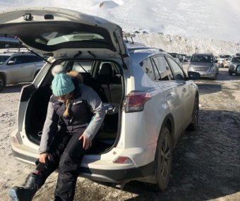 Person sitting in the back of an SUV putting on snow gear in a parking lot