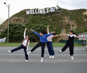 Group of friends jumping playfully in front of the Wellington sign