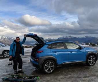 Man standing next to a blue Hyundai SUV with skis in a snowy parking lot