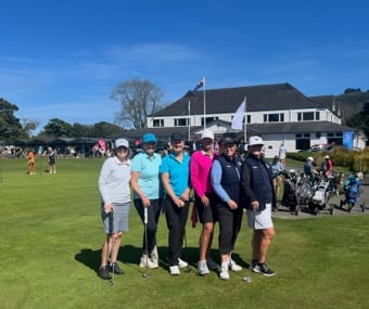 A group of people posing together on a golf course near a clubhouse