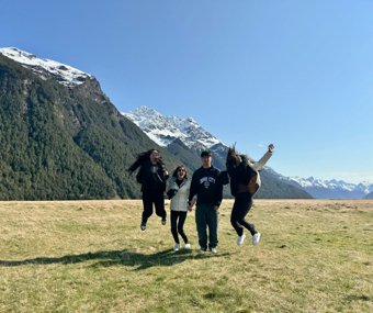 Four friends jumping in a green valley with snow-capped mountains