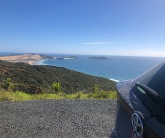 View of the coastline and ocean with a parked car on the roadside