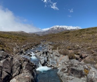 Rocky stream flowing through alpine landscape with a snow-capped mountain in the background