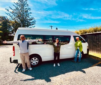 Three people standing beside a white van, arms wide open, on a sunny day