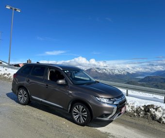 Brown Mitsubishi SUV parked on a snowy road with a mountain view