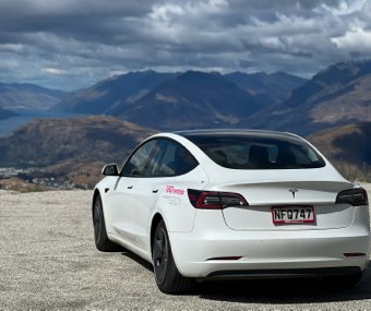 White Tesla parked at a scenic mountain viewpoint under cloudy skies