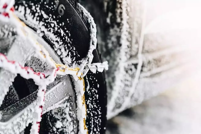 Close-up of a car tire with snow chains covered in ice and snow
